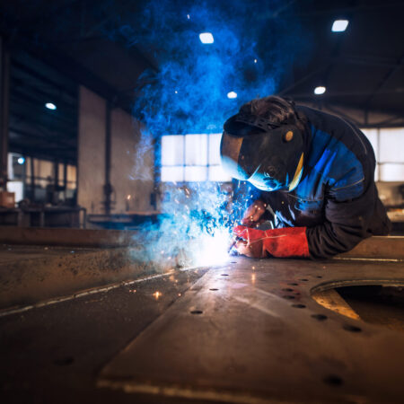 Close up view of worker welding metal construction in industrial workshop.