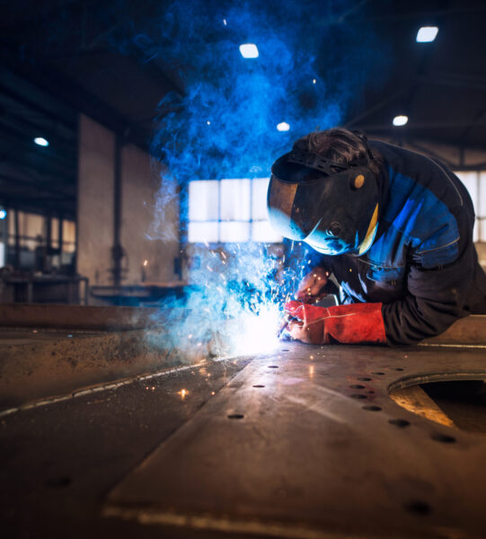 Close up view of worker welding metal construction in industrial workshop.